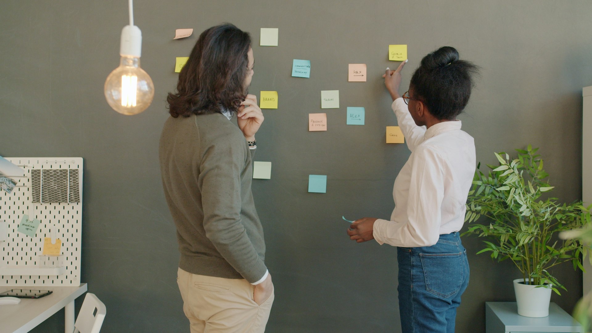 Two people brainstorming with sticky notes on wall.